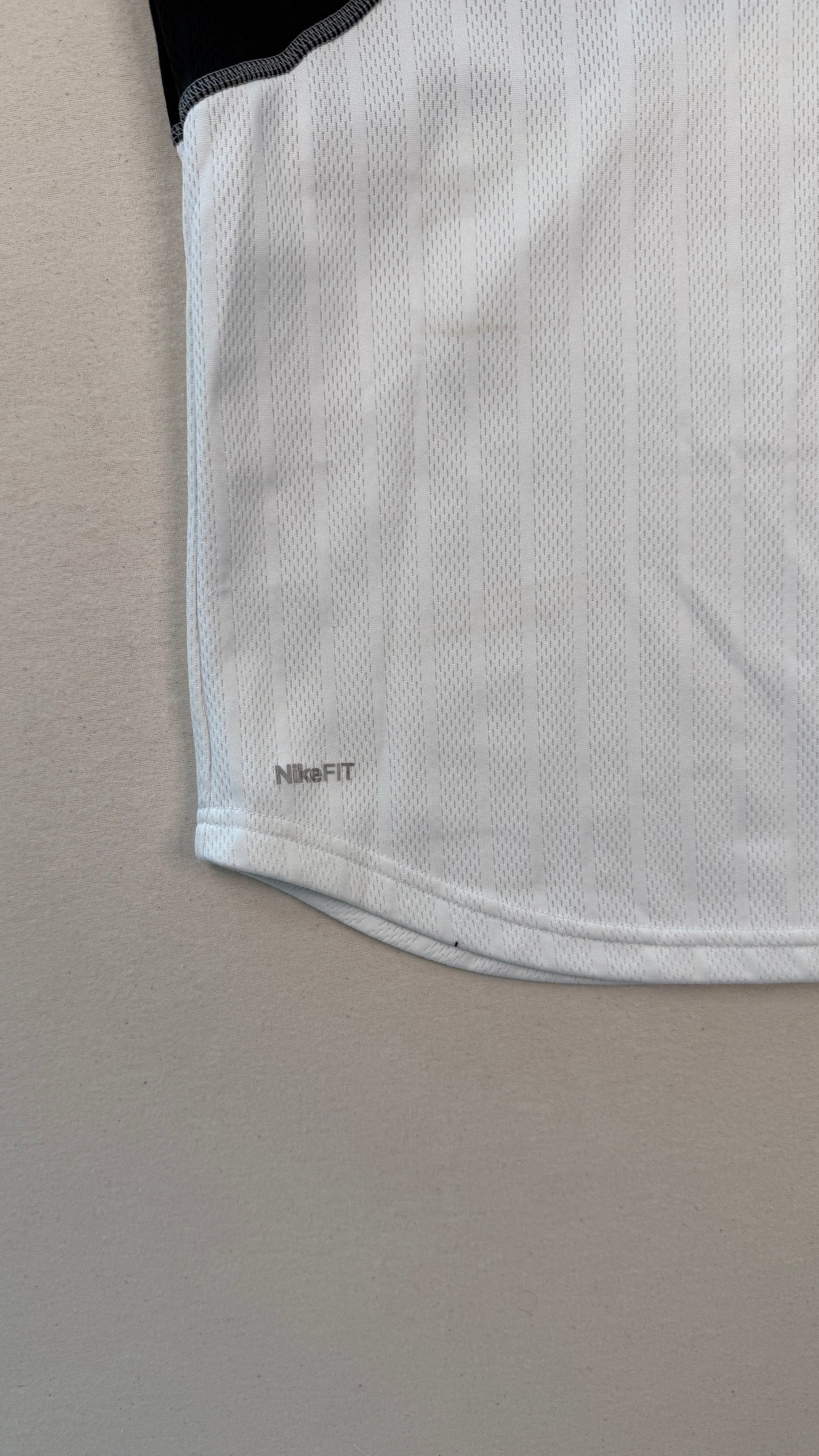 Close-up of a white athletic shirt with black shoulder detail on a beige background