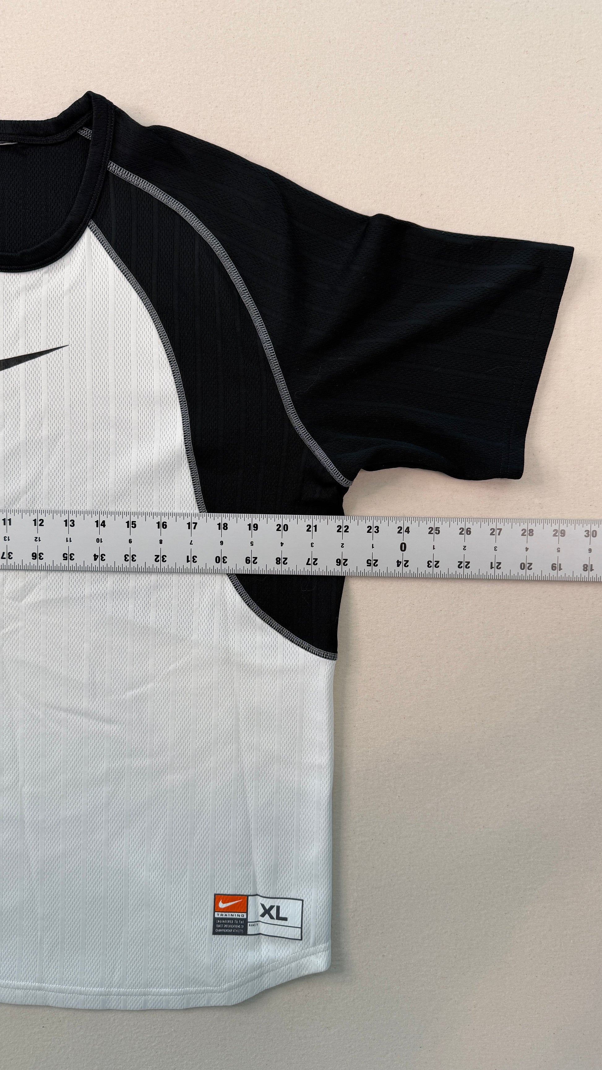 Black and white athletic shirt with a measuring tape for size reference on a beige background