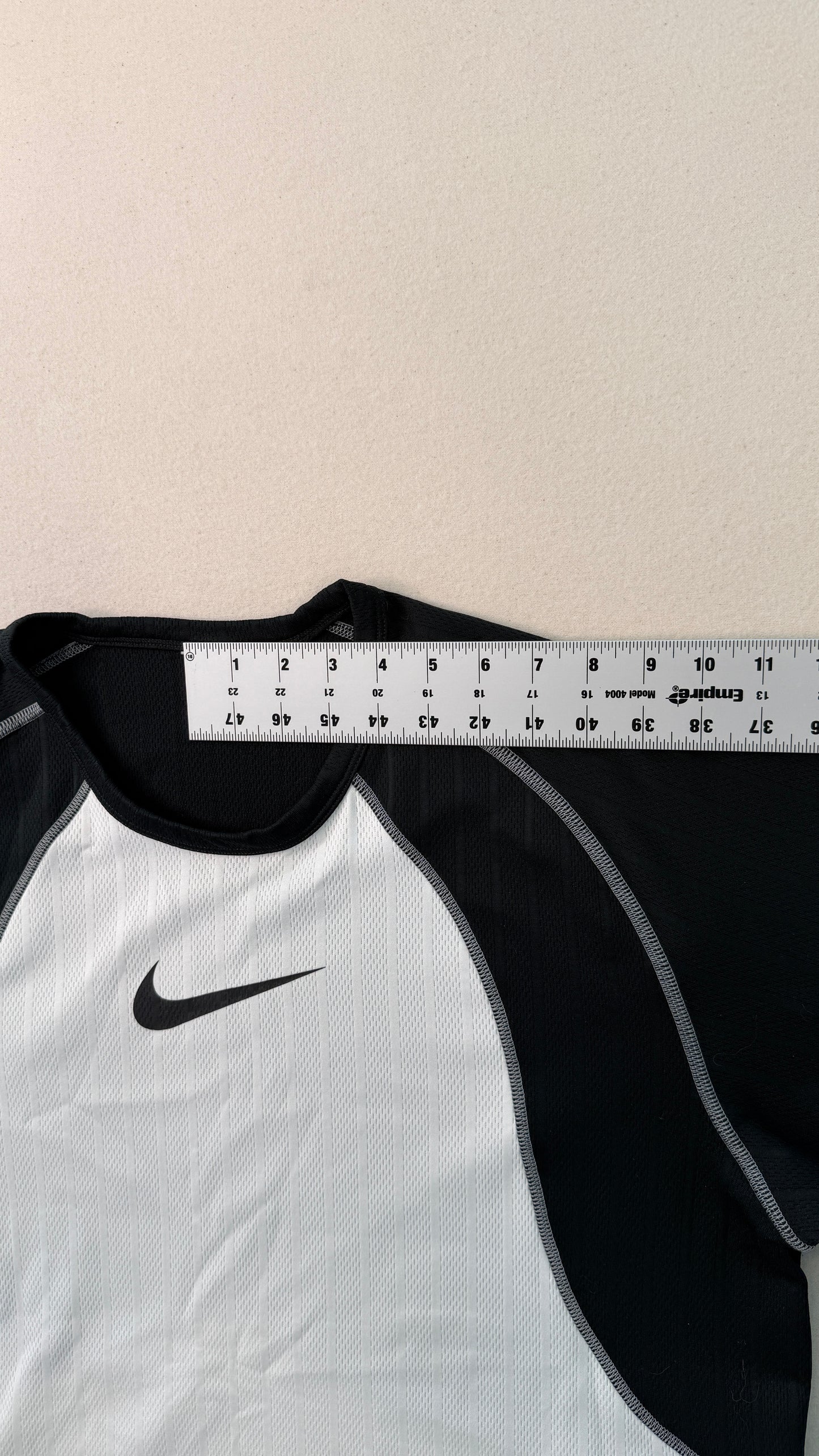 White and black sports shirt with a Nike logo, measured against a ruler on a beige background