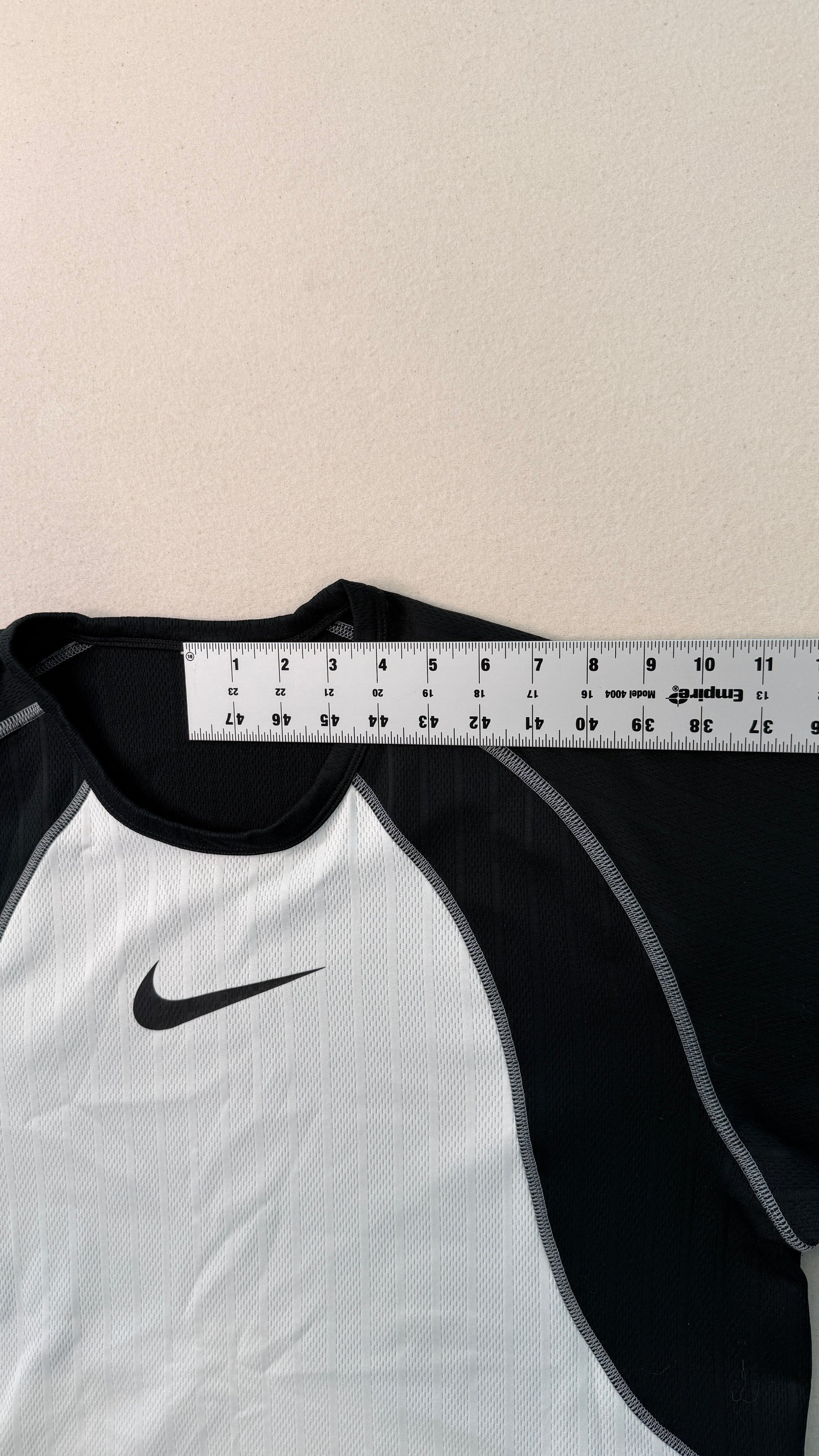 White and black sports shirt with a Nike logo, measured against a ruler on a beige background