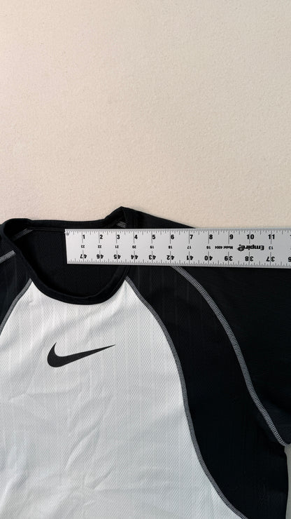 White and black sports shirt with a Nike logo, measured against a ruler on a beige background