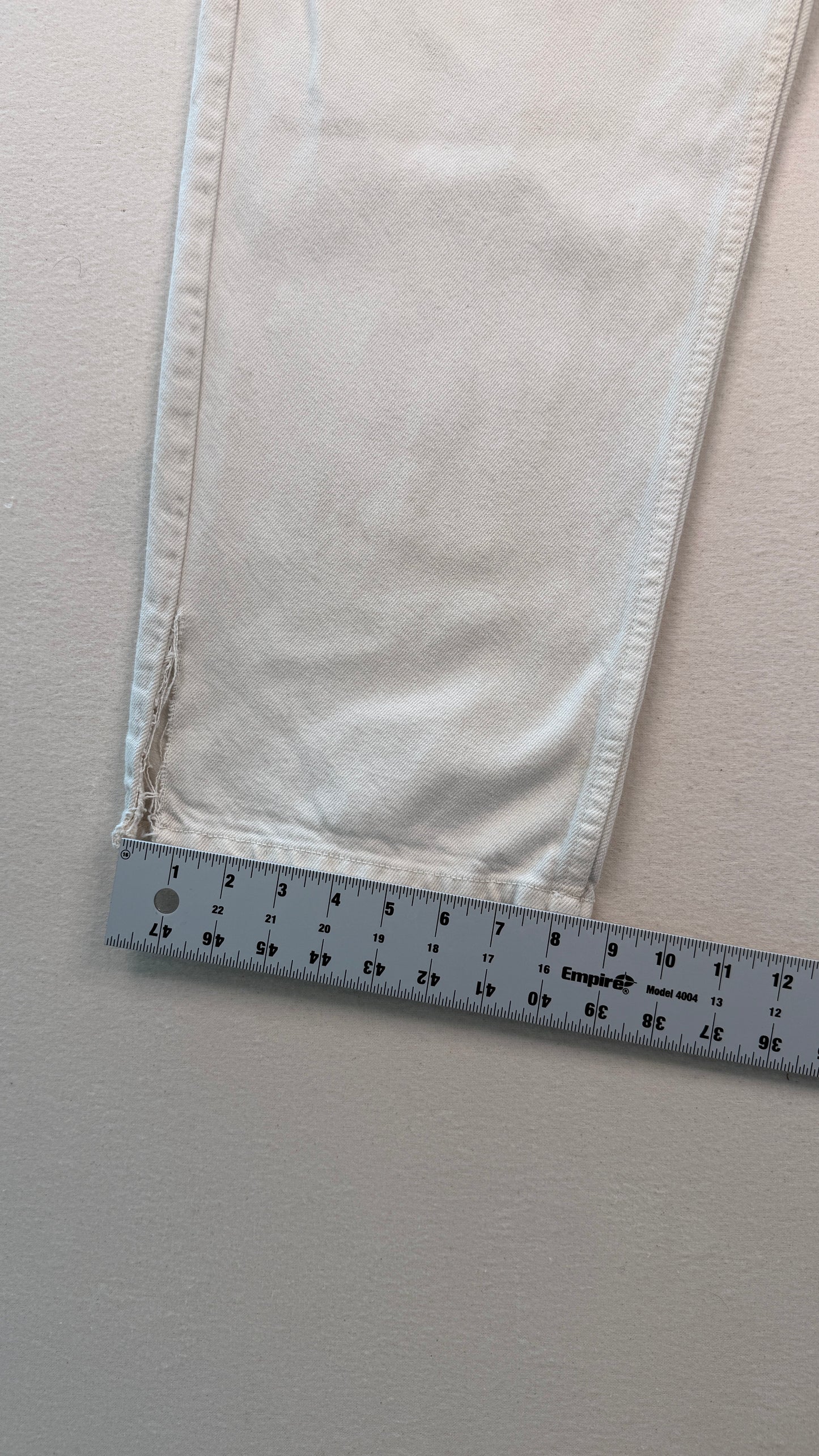 Close-up of light-colored fabric with a ruler at the bottom for scale on a neutral background