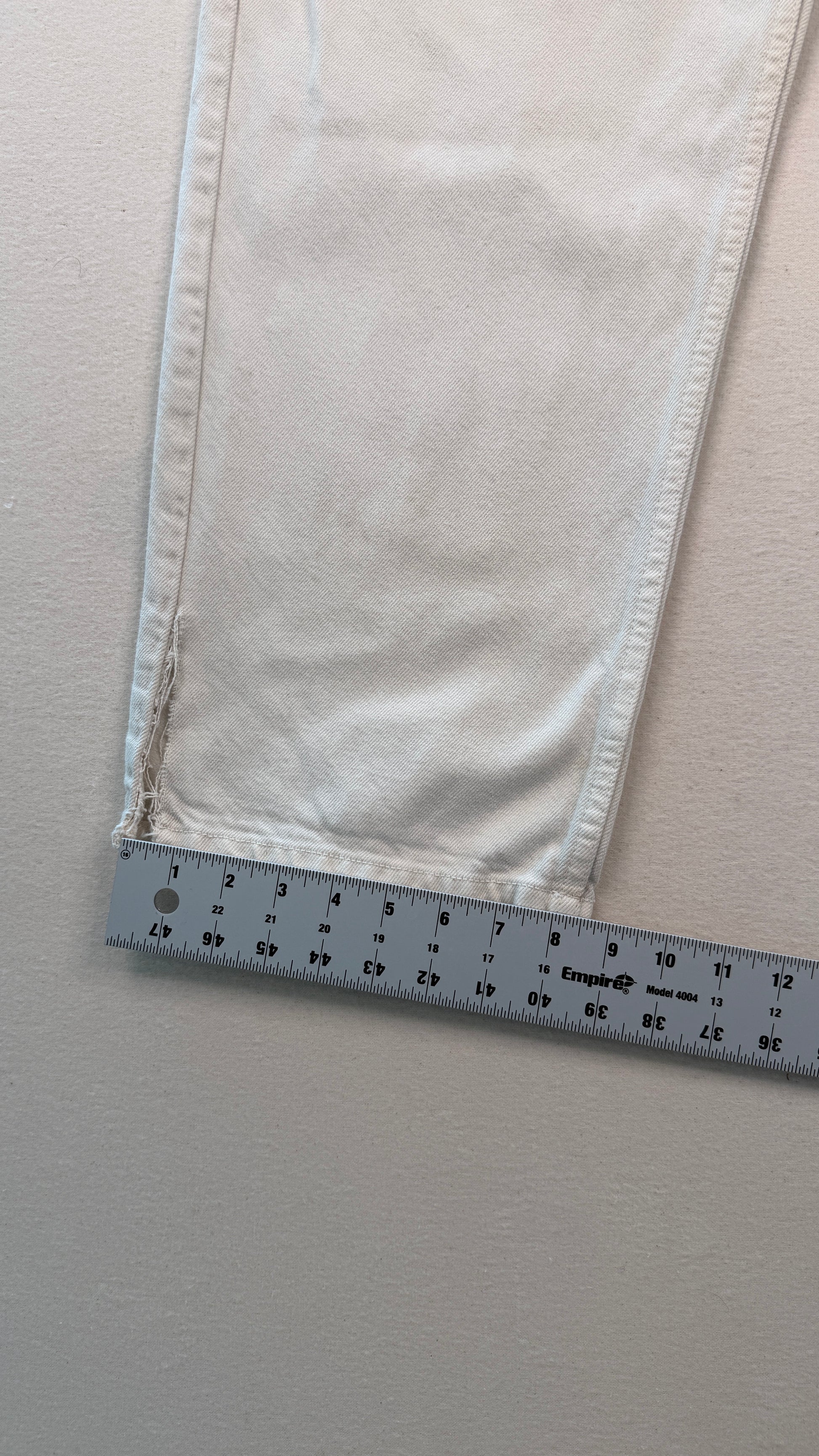Close-up of light-colored fabric with a ruler at the bottom for scale on a neutral background