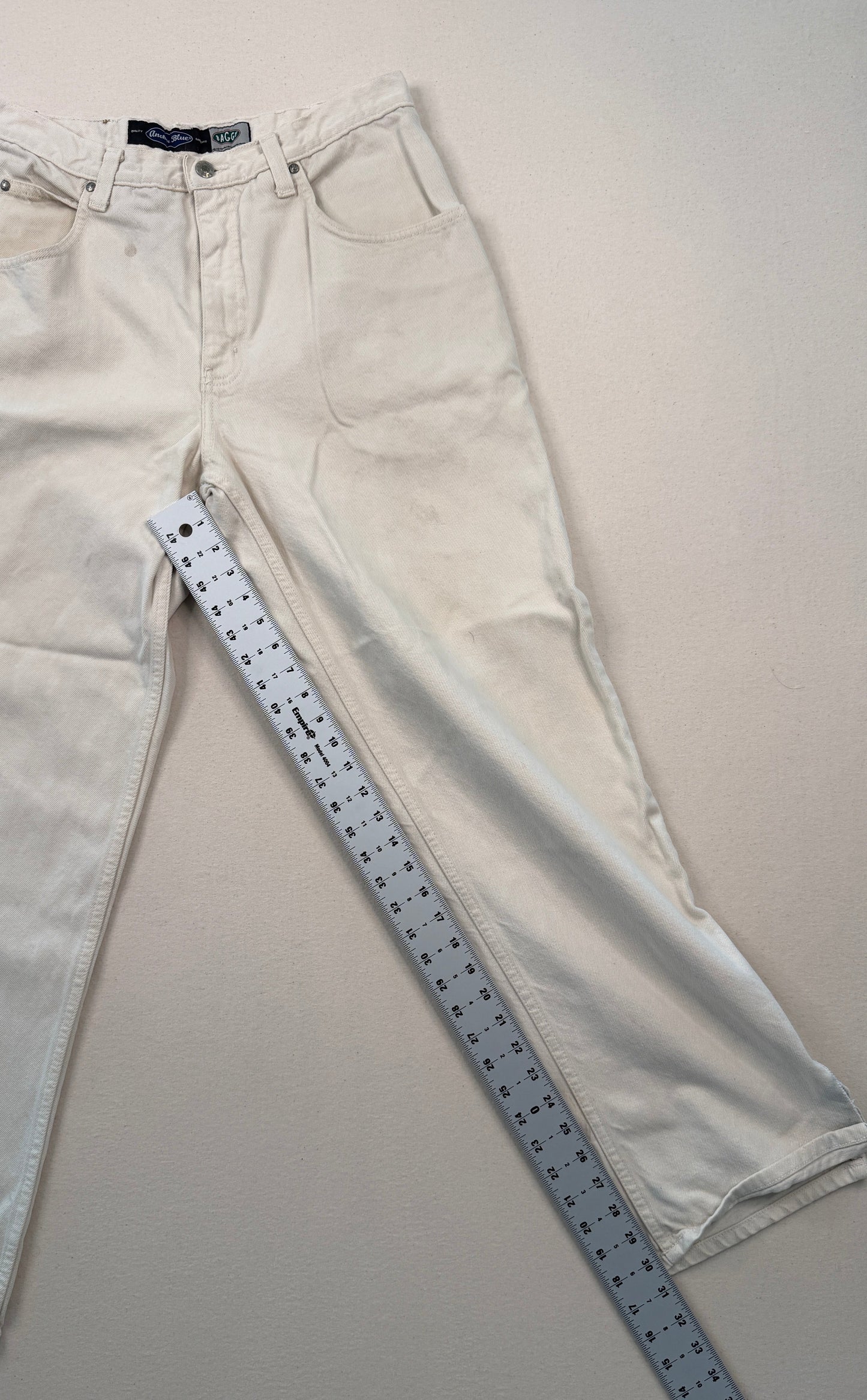 Beige jeans with a ruler for size reference on a plain background