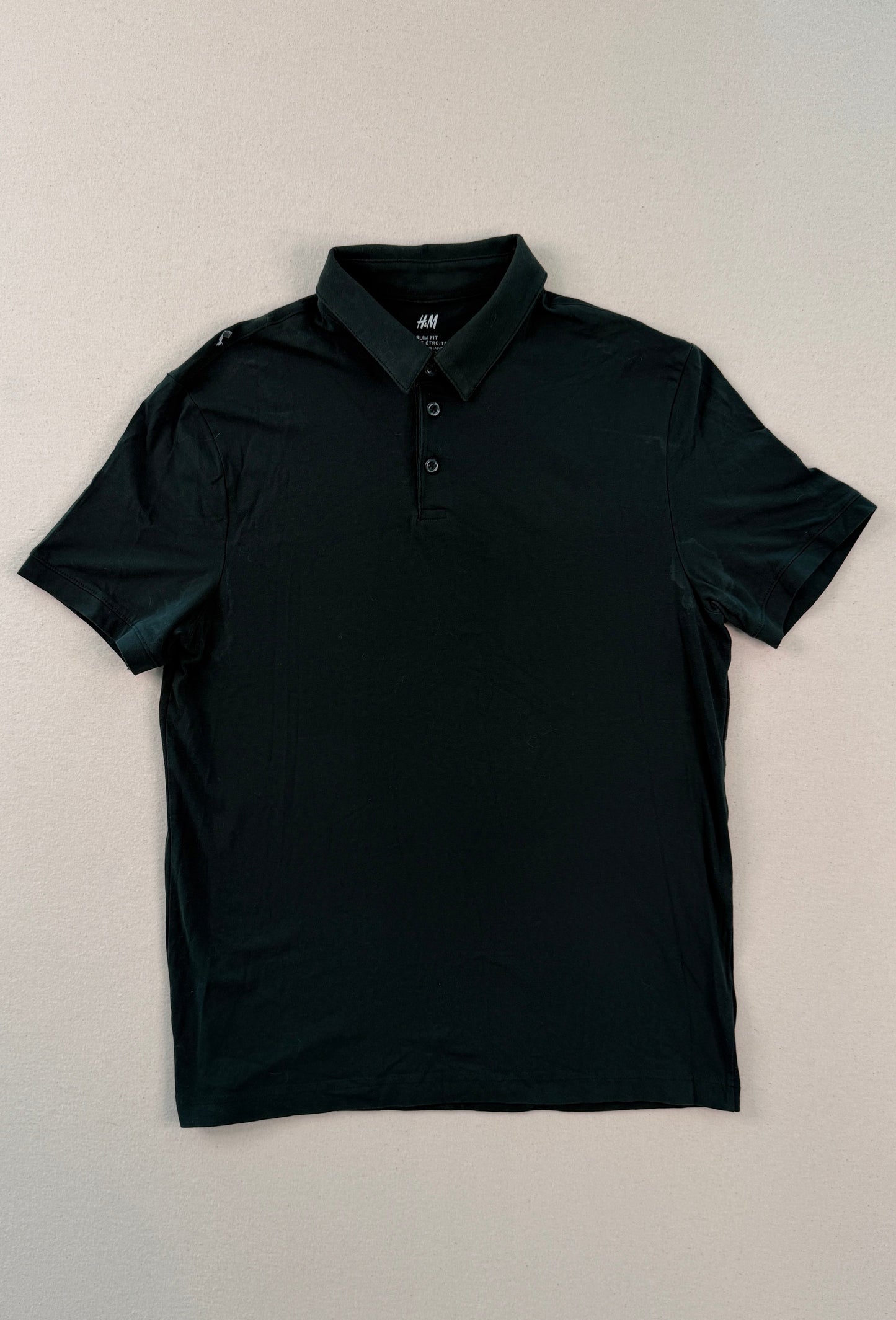 Black polo shirt on a light beige background