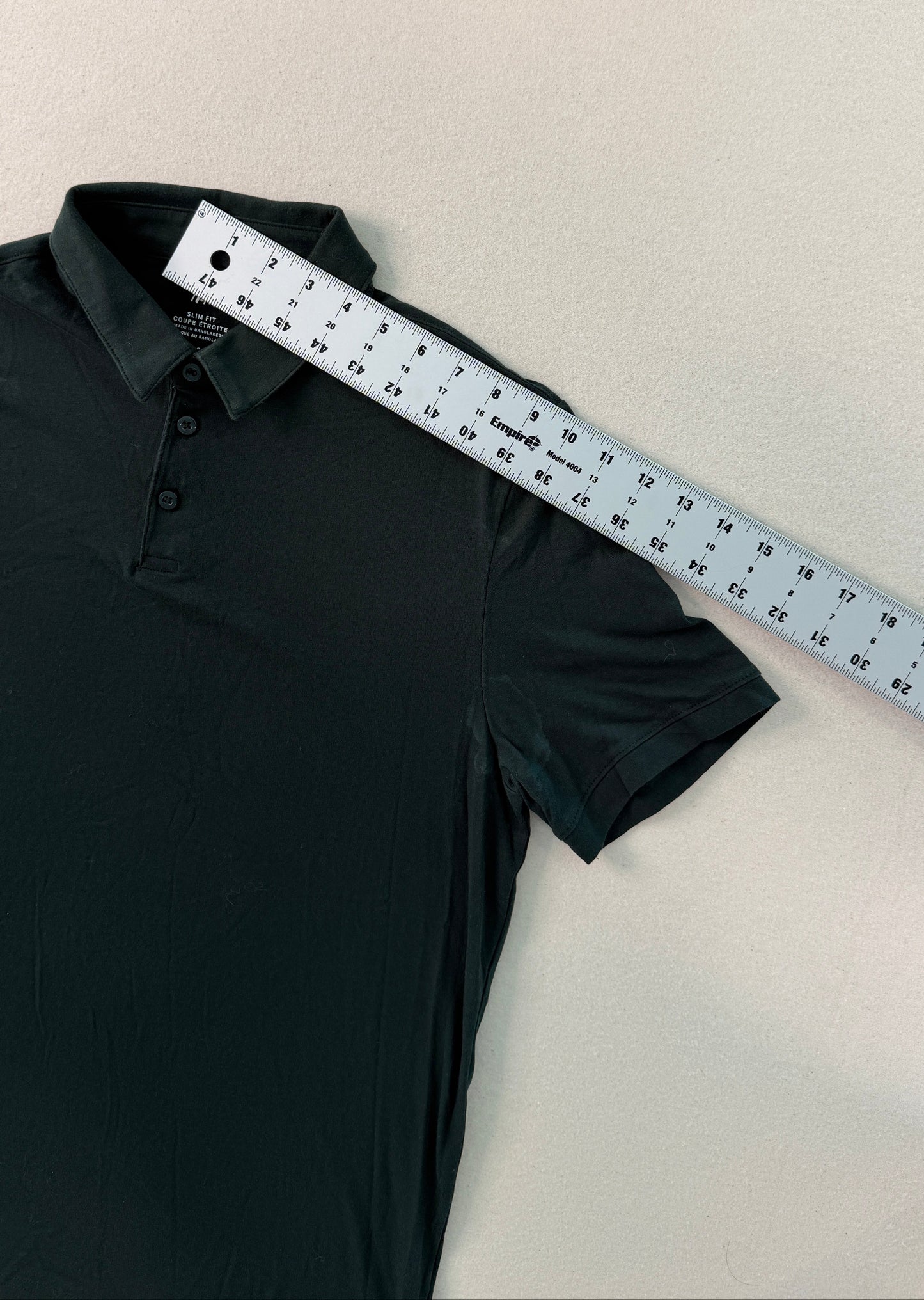 Black polo shirt with a ruler on a beige surface