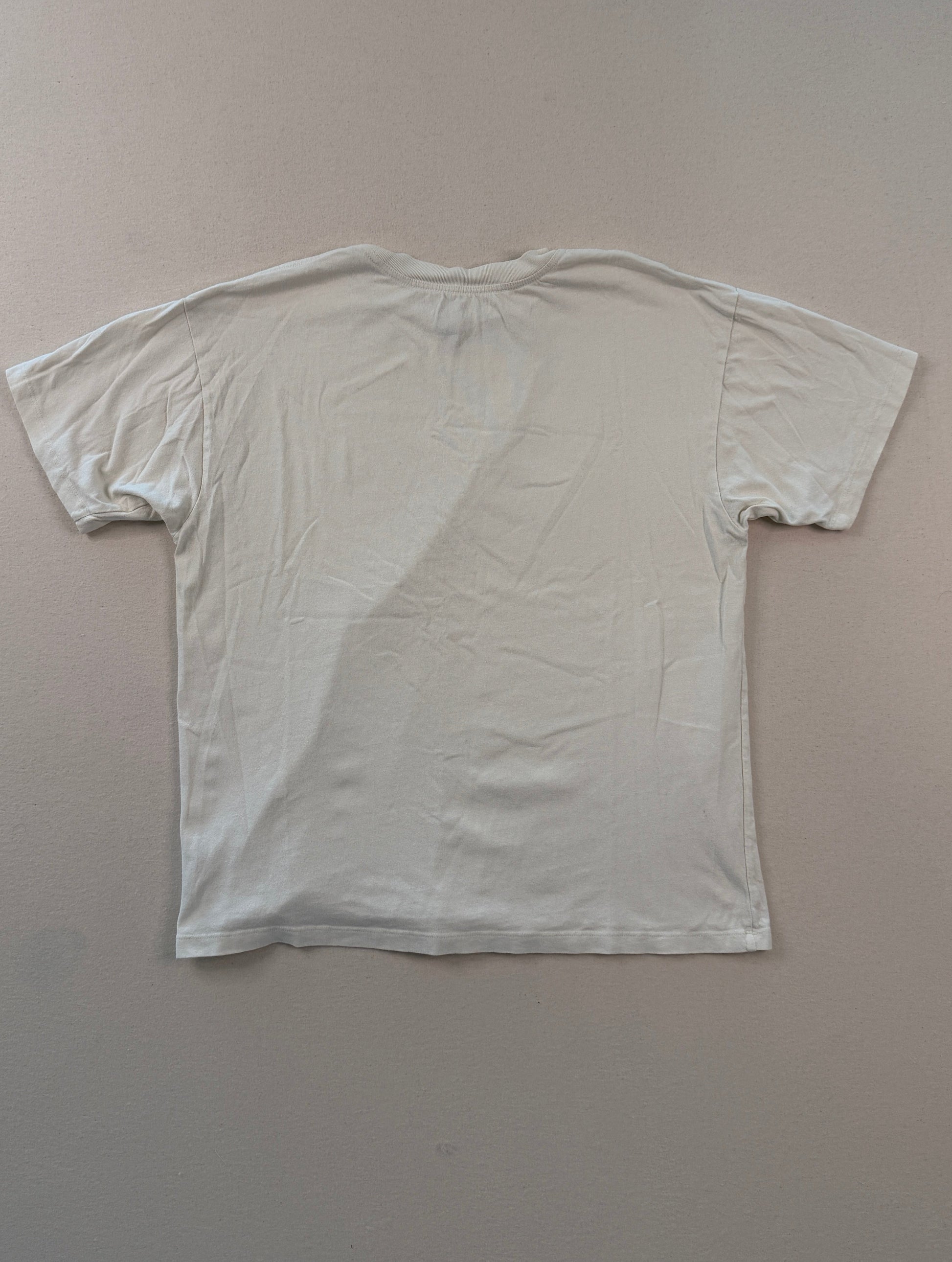White t-shirt on a beige surface with a ruler at the bottom.