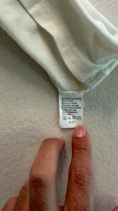 Close-up of a clothing tag on a light-colored fabric with a hand pointing to it.