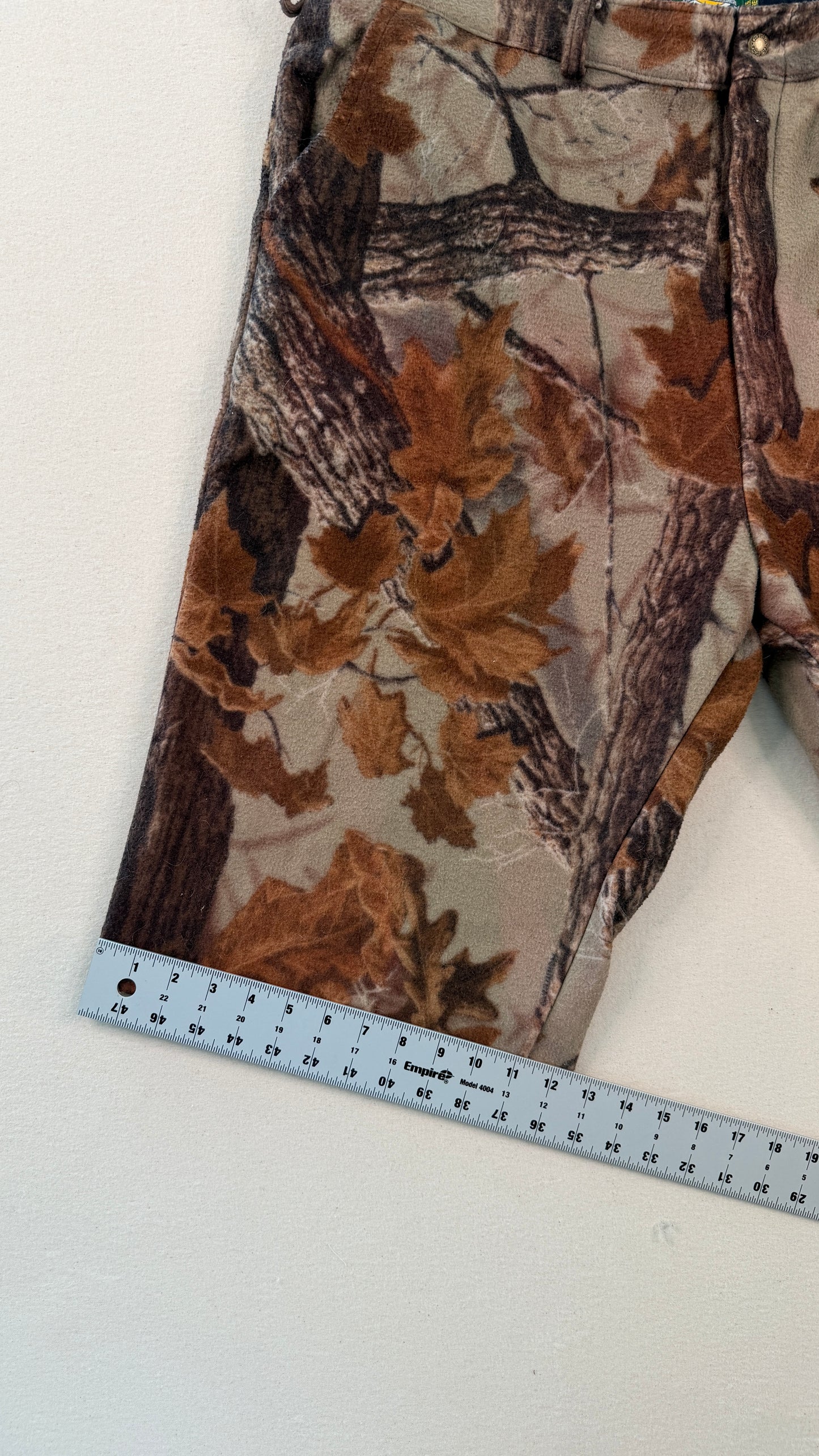 Camouflage-patterned pants with a ruler for scale on a white background